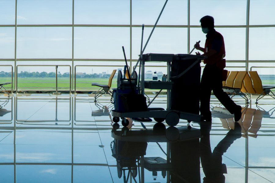 Janitor walking through airport lobby with cleaning cart and supplies