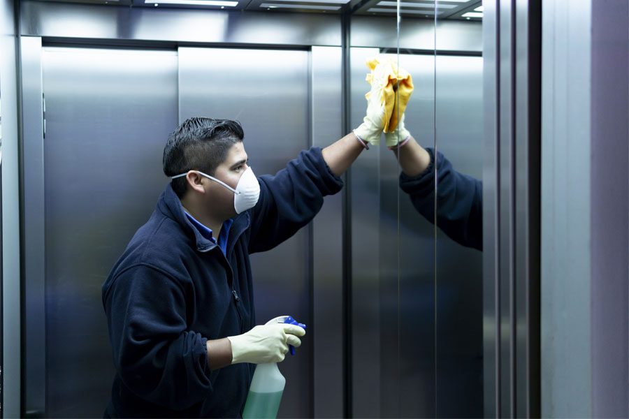 Commercial cleaner in elevator sanitizing and wiping buttons with gloves and a mask
