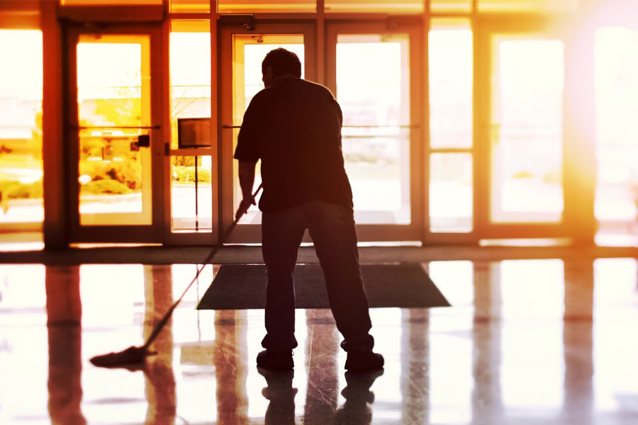 Janitor custodian mopping office floor with sunlight illuminating lobby